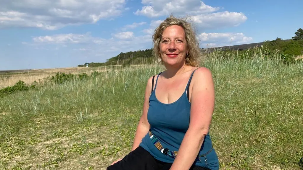 Ein Bild von Miriam Aksoy, der Gründerin von Herz am Fuß, auf einer begrünten Düne am Strand.