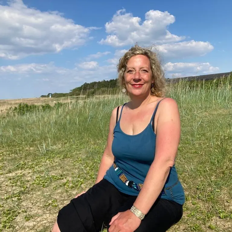 Ein Bild von Miriam Aksoy, der Gründerin von Herz am Fuß, auf einer begrünten Düne am Strand.