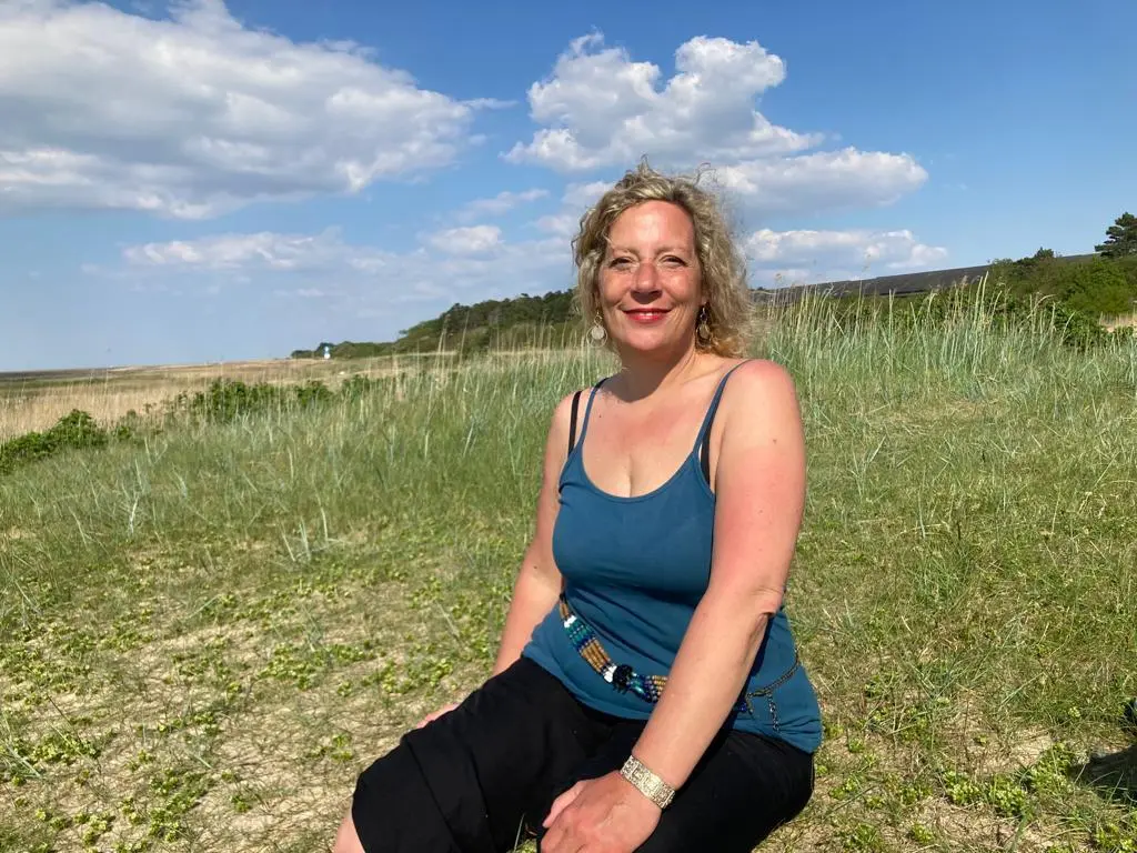 Ein Bild von Miriam Aksoy, der Gründerin von Herz am Fuß, auf einer begrünten Düne am Strand.