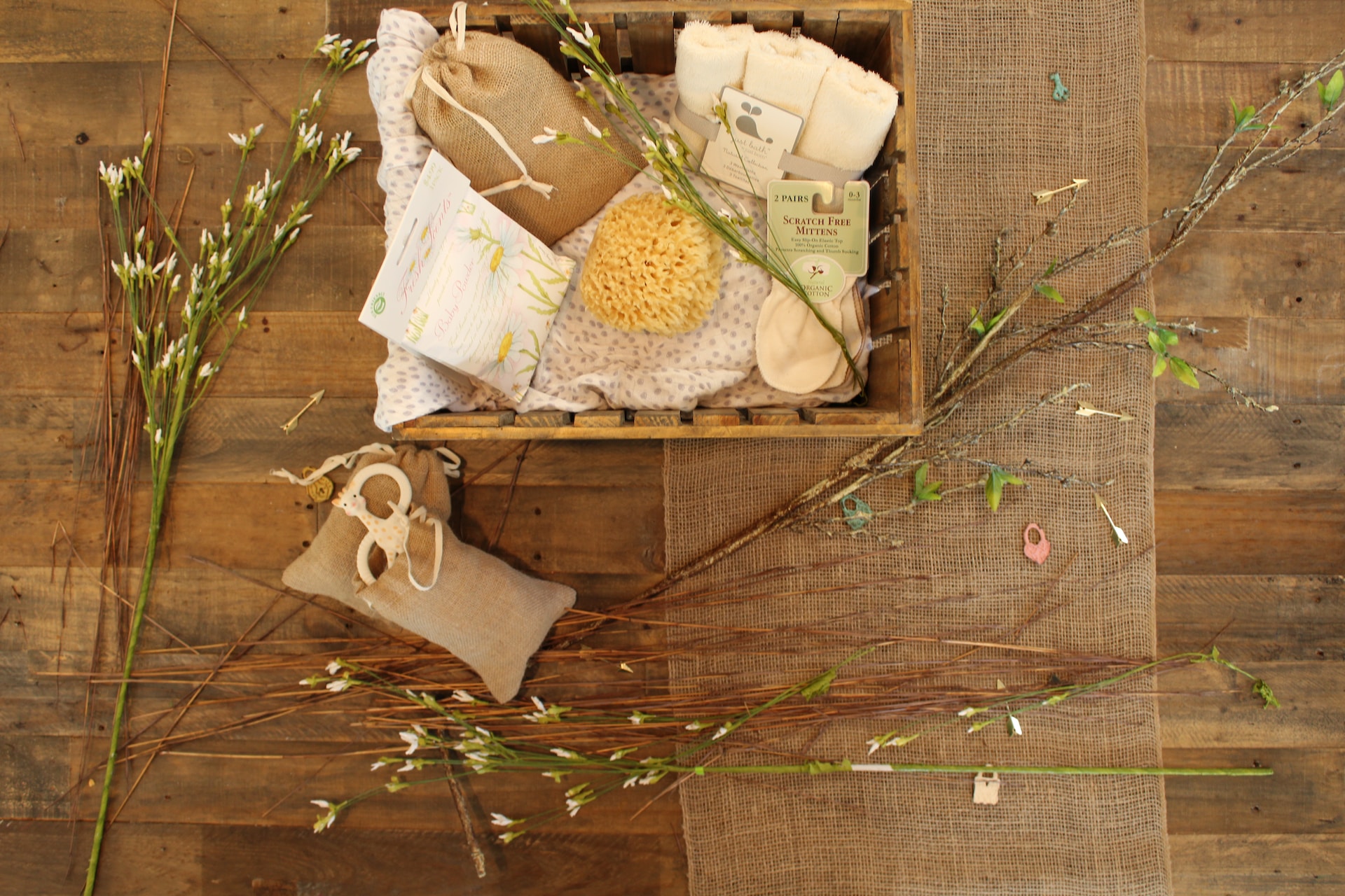 Ein kleiner Korb mit Pflegeprodukten auf einem Holztisch umgeben von einigen Blumenstängeln.