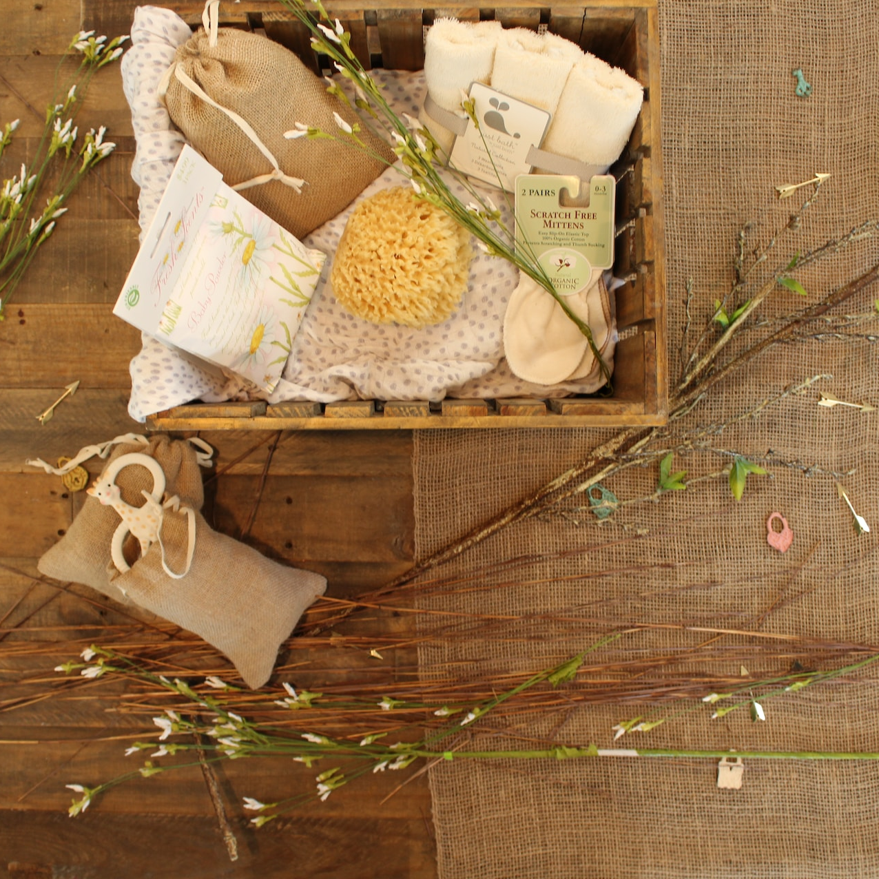 Ein kleiner Korb mit Pflegeprodukten auf einem Holztisch umgeben von einigen Blumenstängeln.